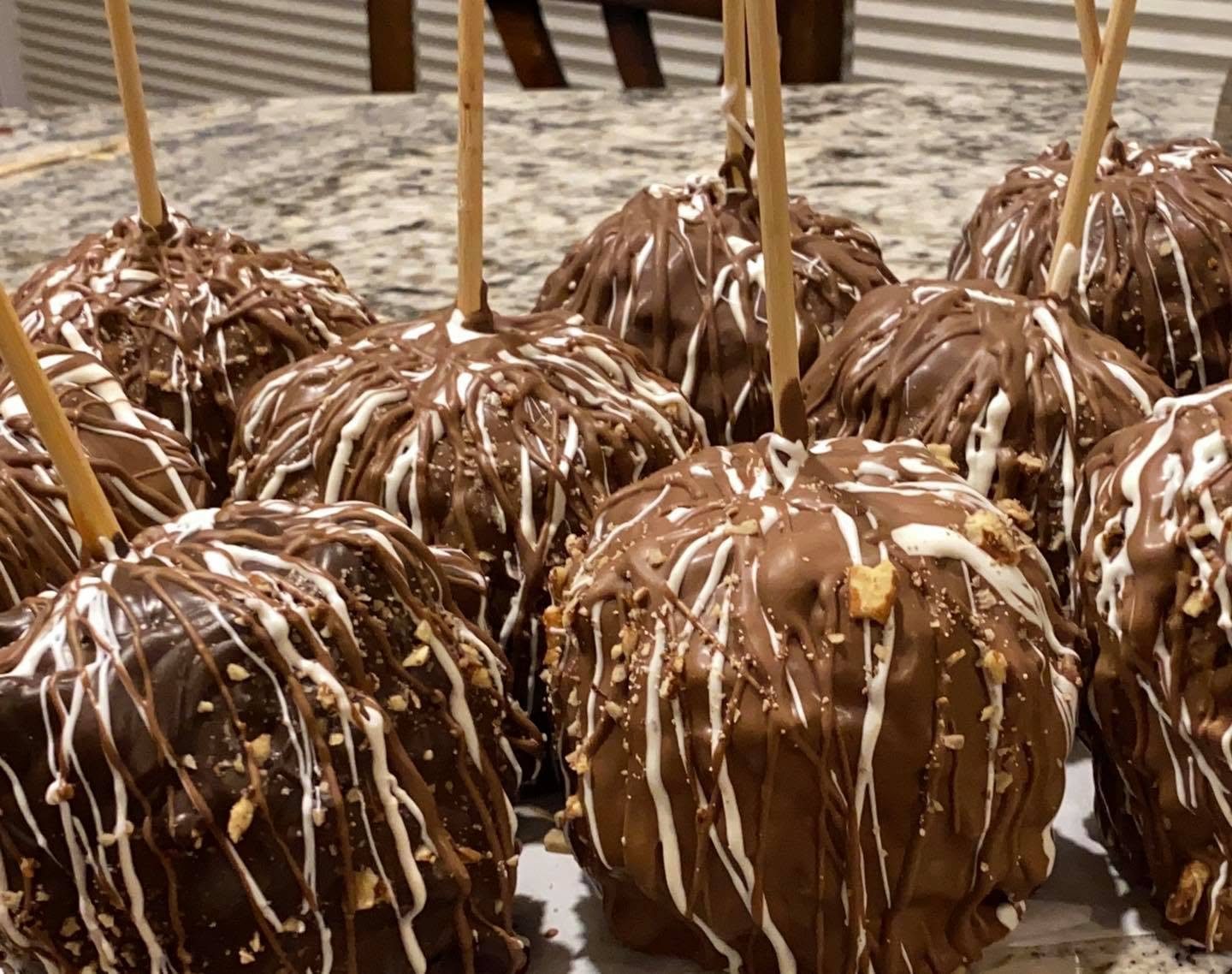 A batch of chocolate caramel apples on sticks with milk and white chocolate drizzle and chopped nuts, on a granite counter