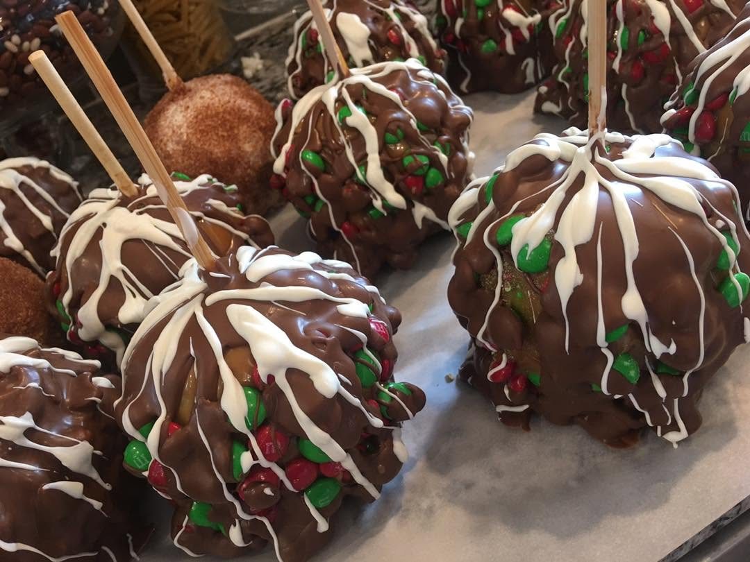 Chocolate caramel apples covered in red and green M&M's with a white drizzle